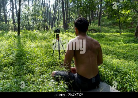 Ragazzo millenario meditando con l'allenatore online tramite la connessione iPad tablet, nella foresta, trasmettendo online la tua classe e le istruzioni, messico Foto Stock