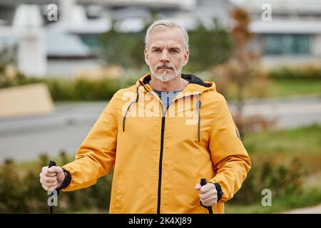 Vita in su ritratto di bel uomo maturo che cammina verso la fotocamera con pali in parco città impostazione, copia spazio Foto Stock