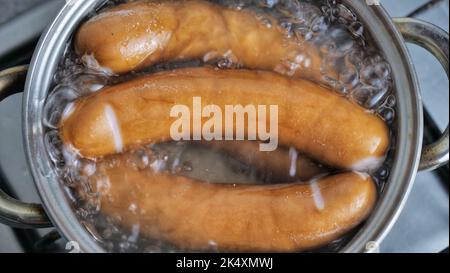 le salsicce vengono cotte in una pentola con acqua bollente. Cuciniamo a casa su una stufa a gas. Foto Stock