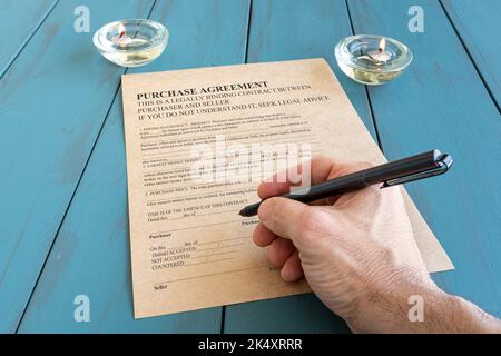 Mano dell'uomo con la penna della fontana che firma il contratto vicino alle candele accese. Foto Stock