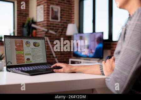 Dipendente donna che analizza i grafici aziendali sul notebook, utilizzando documenti e informazioni di ricerca per creare report sui dati. Lavorare da casa sull'analisi di avvio con grafici web, navigare in internet. Foto Stock