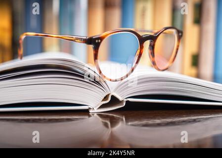 Primo piano sugli occhiali da lettura che si trovano su un libro aperto in biblioteca Foto Stock