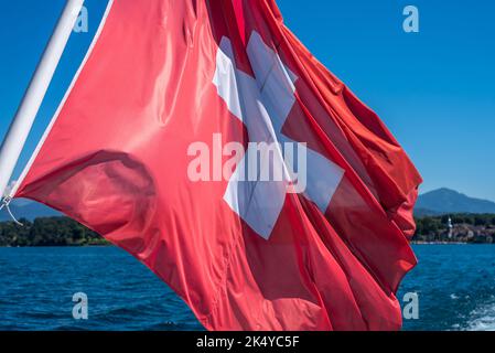 Foto ritratto della bandiera svizzera che batte nel vento da una barca sul lago di Ginevra. Foto Stock