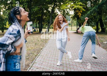 Giovane donna caucasica che spara ai suoi amici ballando nel parco per fare video per i social media, storie di danza alla moda. Comunicazione moderna, sociale Foto Stock