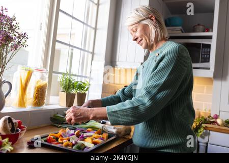 Felice donna caucasica anziana in piedi in cucina e preparare la cena Foto Stock