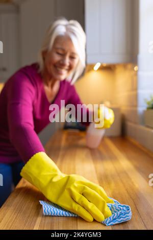 Donna causiana felice che indossa guanti di gomma, pulizia del banco in cucina Foto Stock