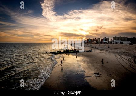 New York, NY - USA - 3 Settembre 2022 Vista orizzontale al tramonto dei navigatori che si godono il surf e la sabbia dell'oceano a Coney Island Beach a Brooklyn. Foto Stock