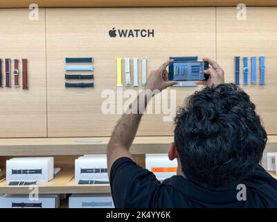Vista posteriore di un uomo indiano scatta una foto del cinturino Apple Watch che viene visualizzato sulla parete all'interno dell'Apple Store Foto Stock