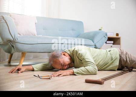 Uomo anziano malato accanto al divano sul tappeto nel soggiorno a casa, nonno anziano maturo che ha un incidente dopo aver fatto la terapia fisica da solo con la passeggiata Foto Stock