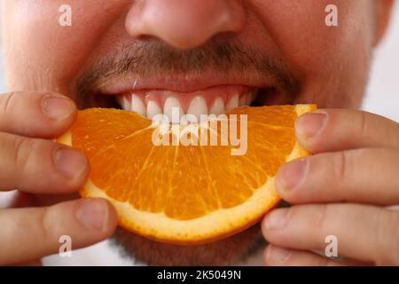 L'uomo sorridente bearded tiene e morde la frutta dell'arancia Foto Stock