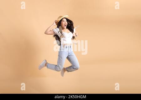 Giovane ragazza asiatica zaino in spalla sorridente e saltando isolato su sfondo beige Foto Stock