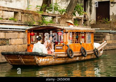 Donne vestite con abiti tradizionali fotografando con i telefoni cellulari su una barca turistica sul fiume Pingjiang lungo Pingjiang Lu una strada piena di o Foto Stock