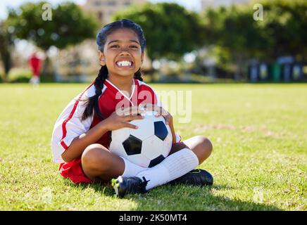 Sport, bambini e ragazze calciatore rilassarsi in erba con palla di calcio, felice ed eccitato al training. Fitness, sorriso e ritratto di bambino indiano su Foto Stock