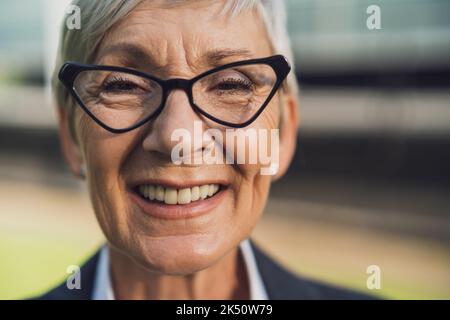 Ritratto della testa all'aperto di una donna d'affari anziana di successo. La persona felice di affari sta sorridendo e guardando la macchina fotografica. Foto Stock