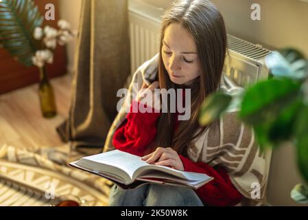 una donna si sta riscaldando al radiatore in una casa fredda, problemi di  riscaldamento, riscaldamento della stanza con un convettore elettrico Foto  stock - Alamy