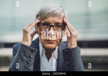 Primo piano ritratto di una donna d'affari anziana che è sovraccarica di lavoro e ha mal di testa. Foto Stock