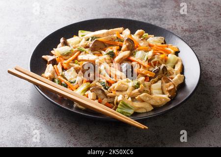 Delizioso soffriggere di pollo tenero e verdure croccanti, tritare il primo piano suey in un piatto sul tavolo. Orizzontale Foto Stock