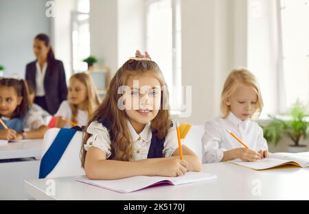 Ritratto di una bella e felice studentessa seduta alla sua scrivania durante la lezione in classe Foto Stock