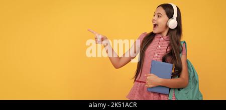 la ragazza teen della scuola stupita nelle cuffie punta il dito sullo spazio della copia, di nuovo alla scuola. Manifesto orizzontale isolato della studentessa della scuola. Intestazione banner Foto Stock
