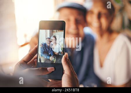 POV, telefono e donna che scattano foto di una coppia anziana al ristorante. Amore, sorriso e anziani, romantico e in pensione abbraccio coppia con la persona che scatta foto per Foto Stock