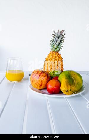 Deliziosa papaia a metà servita sul piatto vicino a frutta colorata assortita e bicchiere di succo d'arancia fresco posto in un tavolo bianco Foto Stock