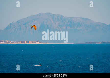 Alto angolo di persona che fa kite surf su acqua turchese ondulazione del mare con montagne sfocate Foto Stock