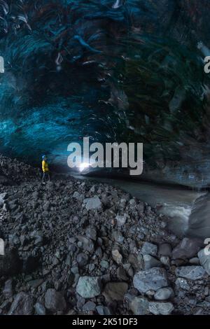Turista in outerwear in piedi vicino a buche irregolari in superficie di ghiaccio, mentre esplorare la grotta nel ghiacciaio Vatnajokull il giorno d'inverno in Islanda Foto Stock