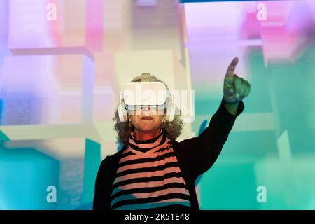 Donna anziana in occhiali e cuffie VR per esplorare il cyberspazio Foto Stock