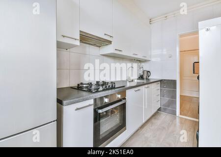 Frammento di interno di piccola cucina domestica con stile minimalista mobili bianchi con lavandino e stufa Foto Stock