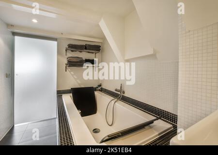 Vasca da bagno in ceramica bianca e WC in bagno illuminato con pareti piastrellate lucide e pavimento in ceramica Foto Stock