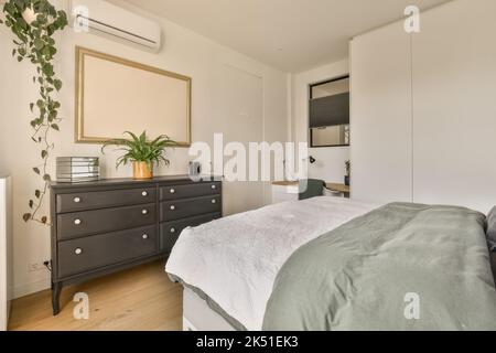 Camera confortevole con letto coperto da soffice piumone vicino al cassettiera e alla scrivania Foto Stock