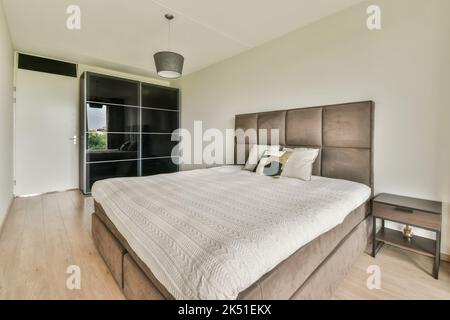 Comodo letto accanto a un armadio nero e pavimento in legno Foto Stock