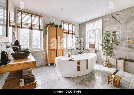 Interni di bagno moderno con decor asiatico, pavimento piastrellato in marmo e vasca ovale bianca accanto a doppio lavabo con armadietti Foto Stock