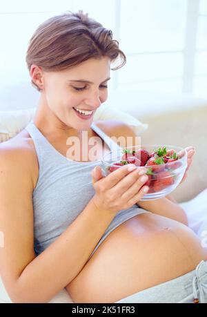 Alcuni nutrienti deliziosi per me e il mio bambino. Una giovane donna felice incinta che tiene una ciotola piena di fragole. Foto Stock