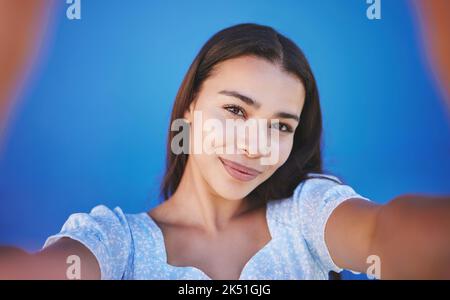 Sorridi, felice e scattando selfie con la donna che mostra il volto durante il viaggio su sfondo blu. POV ritratto di donna sorridente di bellezza naturale Foto Stock