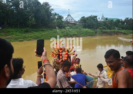 Dimapur, India. 05th Ott 2022. I devoti indù trasportano un idolo della dea Durga per l'immersione nel fiume l'ultimo giorno del festival di Durga Puja, come due chiese sono viste dietro, al fiume Dhansari in Dimapur, stato nord orientale dell'India di Nagaland. Durga Puja commemora l'uccisione del re demone Mahishasur da parte della dea Durga, segnando il trionfo del bene sul male. Credit: Caisii Mao/Alamy Live News Foto Stock