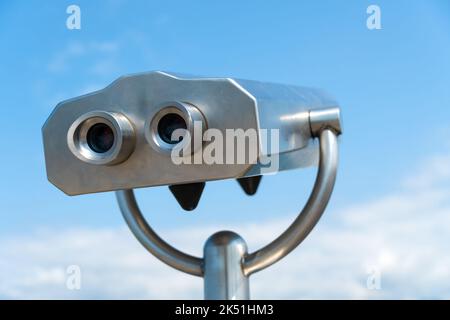 Primo piano di un binocolo fisso grigio metallo sulla piattaforma di osservazione contro il cielo blu in una giornata di sole. Bizzarro immaginario uomo metallo Foto Stock