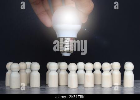 Bambole in legno e lampadina. Brainstorming, progetto comune, innovazione, cooperazione. Creatività e ingegnosità. Processo di pensiero e concetto di idee Foto Stock