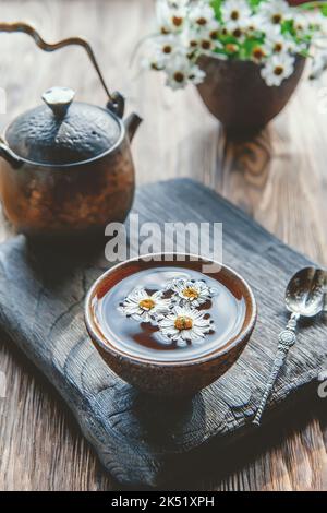 Tè a base di fiori di camomilla freschi. Bevanda calda, medicina alternativa. Sfondo di vecchie tavole di legno, primo piano Foto Stock