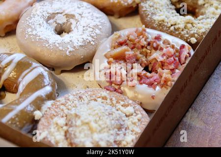 Immagine di ciambelle assortite in una scatola con ciambelle al cioccolato, in polvere e cosparse di pancetta. Foto Stock