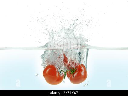 Tre pomodori che spruzzano in acqua. Vista laterale su sfondo bianco. Foto Stock