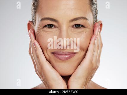 Donna anziana, viso e cura della pelle sorridono per la bellezza che tocca la pelle morbida e liscia su uno sfondo studio. Primo piano di una donna anziana isolata Foto Stock