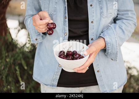 Mani di una donna anziana che tiene una ciotola di ciliegie mature Foto Stock