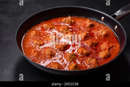 Deliziose polpette di carne macinata in salsa di pomodoro piccante servite in una padella nera Foto Stock