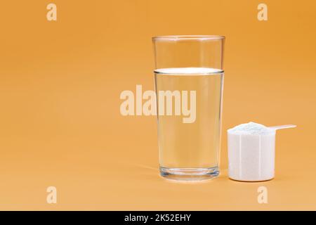 cucchiaio di polvere di collagene idrolizzato, con vetro d'acqua, proteine per l'elasticità della pelle, fondo isolato e copyspace Foto Stock