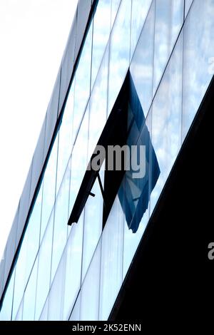 Astratto architettonico - una finestra aperta su un edificio con facciata in vetro con riflessi del cielo, vista ad angolo basso Foto Stock