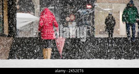 Belgrado, Serbia - 15 dicembre 2018: Donna che indossa parka rossa e che tiene l'ombrello e altri pedoni che camminano per la strada cittadina in una giornata nevosa Foto Stock