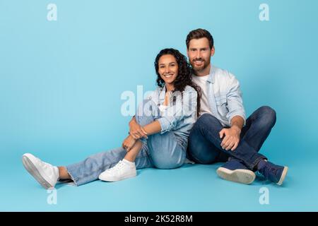 Sorridente carpine millennial europeo maschio e donna araba, siede sul pavimento, godere di tempo libero Foto Stock