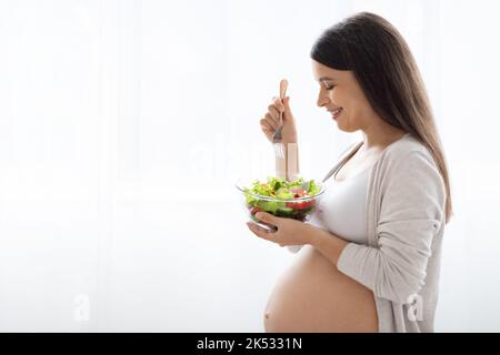 Felice donna incinta che tiene ciotola con insalata di verdure fresche Foto Stock