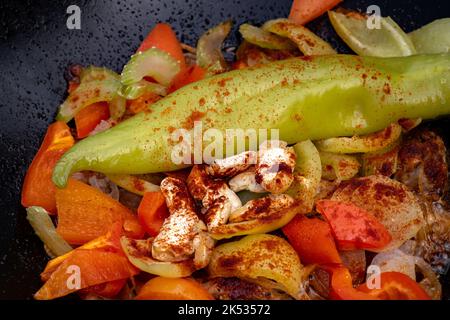 Grandi pezzi di verdure asiatiche e carne fritti in olio con bolle in un primo piano di cottura nero calderone Foto Stock